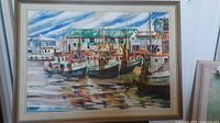 Framed painting showing a harbor with several boats docked and buildings in the background.