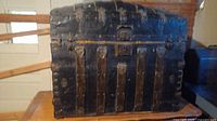 Front view of large black vintage steamer trunk with metal hardware and leather straps showing age wear.