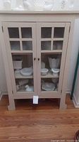 Front view of a wooden storage cabinet with glass paneled doors, closed, showing contents inside.