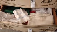 Drawer partially open showing a variety of folded table linens including embroidered napkins and folded runners