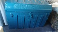 Full view of the painted blue metal steamer trunk showing embossed decorative details and overall shape
