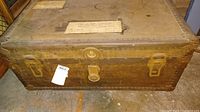 Front view of the vintage large trunk showing metal latches, lock, and riveted edges with a worn surface.