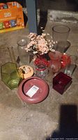 Full assortment of vases in various shapes, sizes, and colors arranged on the floor including glass and ceramic types, some with artificial flowers.