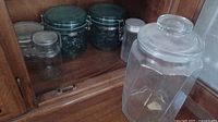 Display of various vintage glass jars on wooden shelf including different lid types and sizes.