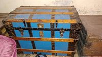 Front view of vintage steamer trunk showing blue panels, wood slats, metal edges, and latches.