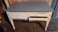 Front view of vintage painted wooden farm table showing two drawers with one difficult to open and turned legs.