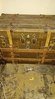 Front exterior of vintage wooden trunk with metal reinforcements and leather straps.