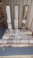 Eight rolls of peel and stick wallpaper including floral and stone patterns arranged on a surface and standing upright