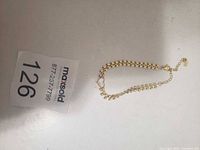 Gold plated heart bracelet on tabletop beside MaxSold tag
