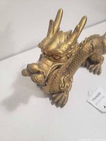 Front view of gold-tone Chinese dragon figurine showing horned head and front legs