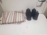 Folded striped curtains next to four black thread cones on table