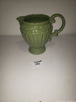 Front view of green ceramic water jug showing embossed details and handle