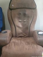 Front view of the brown massage recliner chair showing the seat, backrest, armrests, and visible wear marks on the upholstery.