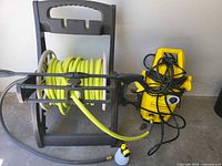 Photo showing electric pressure washer, hose reel with garden hose, spray gun, and foam sprayer on concrete floor against gray wall