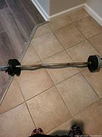 Photo of an adjustable EZ curl barbell with multiple black-coated metal weight plates on each end, set on a tiled floor.