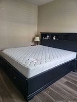 Full view of king size black platform bed frame with mattress, showing headboard shelves and base drawers.