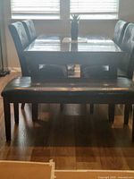 Photo showing the dark base dining table with stone top, four padded faux leather chairs, and matching faux leather bench in front.