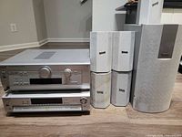 Front view of Panasonic home theater system components including receiver, DVD player, 5 surround speakers and subwoofer arranged on wooden floor.