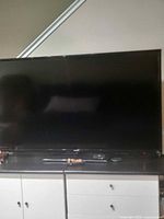 Front view of the Samsung 55-inch flat screen TV powered off, showing entire screen and part of the stand with cables.