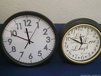 Photo shows two distinct wall clocks side by side: Westclox branded clock with simple numeric dial and a decorative 'Live Laugh Love' clock with script numbers and gold trim on black frame.
