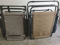 Two folded zero gravity folding lounge chairs side by side, showing back panels with mesh fabric and metal frame in black finish.