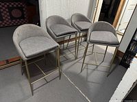 Four matching gray upholstered bar chairs with gold metal legs