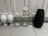 All six items lined up: pair white eggs, three clear glass vases, black ribbed vase