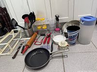 Full lot overview on kitchen floor showing pan, utensils, holder, rolling pin, spice jars, bagel holder, plastic wrap, knife etc.