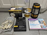 Group shot of all items: two lanterns, SmartLight timer box, NXT charger box, window insulation kit box, bag of telephone couplers