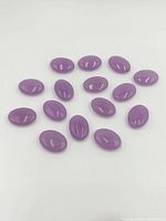 Top view of 18 oval amethyst cabochon beads arranged on white background.