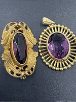 Photo showing the amethyst brooch and pendant set side by side on a dark background highlighting details of the stones and frames.