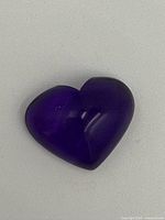 Heart-shaped amethyst gemstone with deep purple color, smooth polished surface shown from one angle.