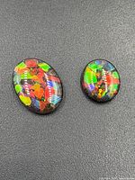 Two oval cabochon ammolite gemstones on black background showing vibrant multi-color iridescence and polished finish.