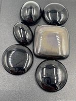 Six polished black cabochon stones including round, oval, and square shapes on a dark background.