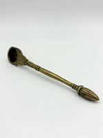 Brass ritual spoon photographed from an oblique angle showing the carved handle and bowl.