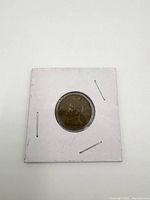 Front side of the first vintage coin secured in a white cardboard holder with staples