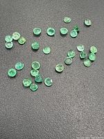 Multiple small loose emerald gemstones scattered on a black surface showing color and size variations.