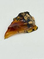 Angled side view of the fire opal shard showing translucent orange hues and beige-black mineral inclusions.
