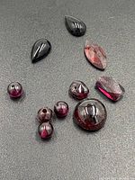Garnet gemstones in various shapes and cuts including pear, marquise, round cabochons and beads on black background.