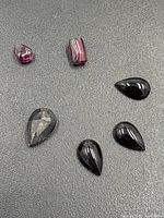 Garnet gemstones in different shapes and colors on dark background, including pear-shaped and rectangular cuts.