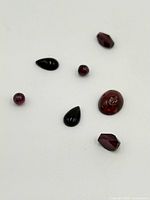 Seven loose garnet gemstones placed on white background, various cuts and sizes shown