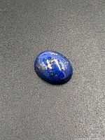 Oval polished lapis lazuli cabochon stone with visible pyrite flecks on dark surface.
