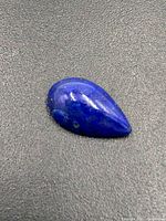 First close-up photo of a pear-shaped polished lapis lazuli gemstone showing deep blue color with lighter veins and patches.