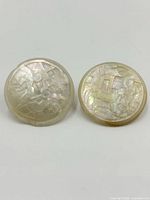 Front view of pair of round mother of pearl stud earrings with carved geometric patterns.