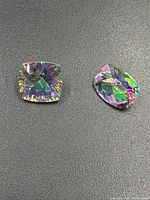 Two cushion-shaped mystic topaz gemstones showing iridescent colors on a dark background.