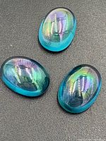 Three oval cabochon cut mystic topaz gemstones with iridescent colors including blue, green, and purple.