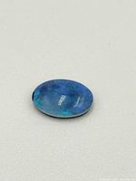 Polished oval opal gemstone showing a mix of blue and green hues on a plain light background.