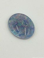 Close-up image of an oval cabochon opal gemstone showing vibrant multi-color iridescence and polished smooth dome surface, placed on a white background.