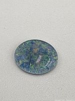 Close-up image of polished oval cabochon cut opal gemstone showing blue, green, and orange color play.
