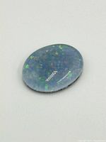 Close-up image of a single polished opal gemstone displaying green and blue iridescence on a white background.